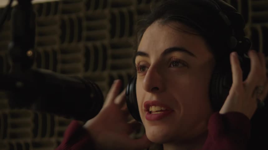 A female voice artist puts on headphones and begins speaking into a microphone in a professional recording studio