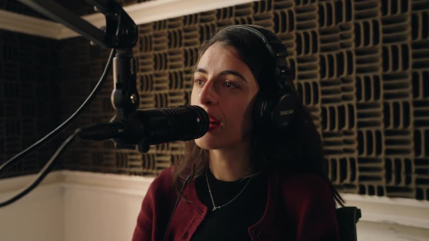A woman with headphones speaks into a professional microphone while recording a podcast in a soundproof studio