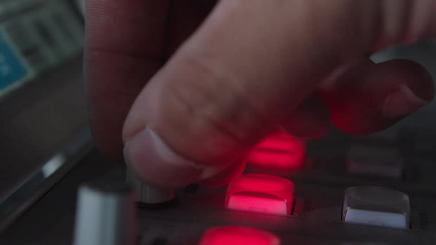 A close-up of a person's hand adjusting a knob on a sound mixing board with glowing red lights