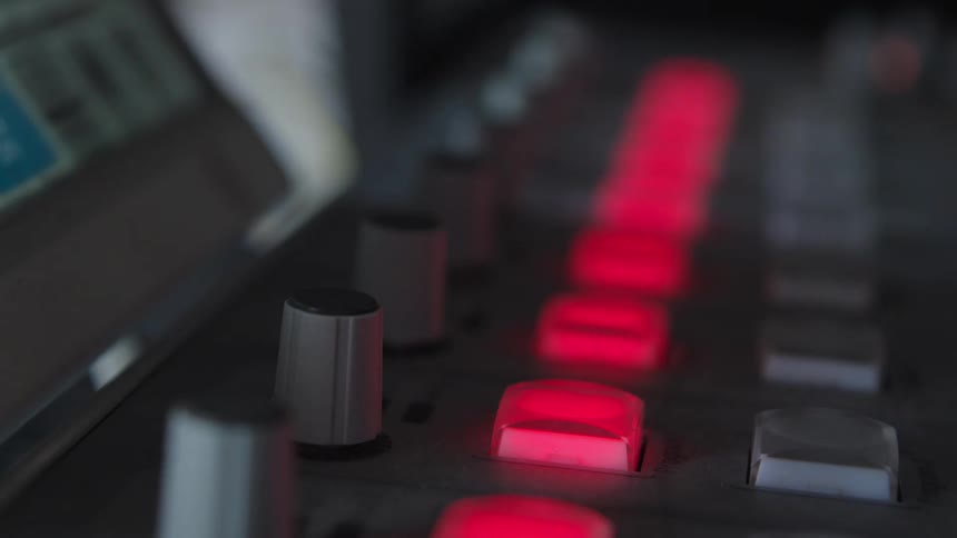 A close-up shot of a finger with glitter nail polish repeatedly pressing a glowing red button on a professional control board
