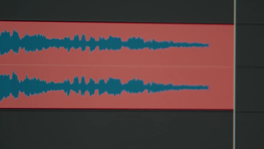 Close-up of a blue stereo audio waveform playing back on a red track within a digital editing software timeline
