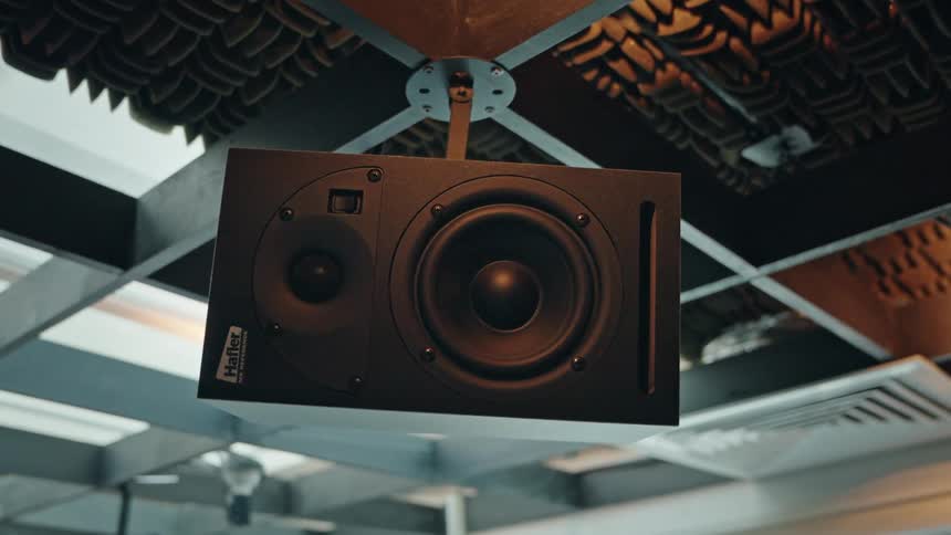A low angle close-up of a professional black studio monitor vibrating as it plays music in a soundproofed recording booth
