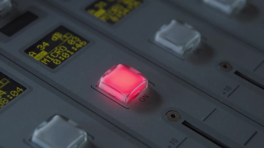 A radio host pushes the 'ON' button for the microphone on an audio mixing console, and it lights up red