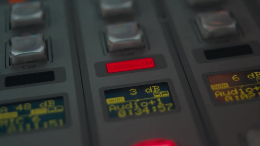 Close-up of a digital audio mixer with a glowing red 'channel on' button and running timecode