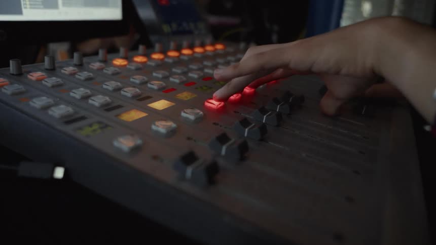 A sound engineer's hands expertly operate a professional audio mixing console in a dimly lit studio