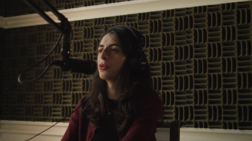 A woman wearing headphones speaks into a professional microphone while recording a podcast in a soundproof studio