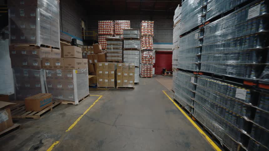 Slow push-in shot through a large industrial warehouse filled with pallets of boxes and inventory ready for shipping
