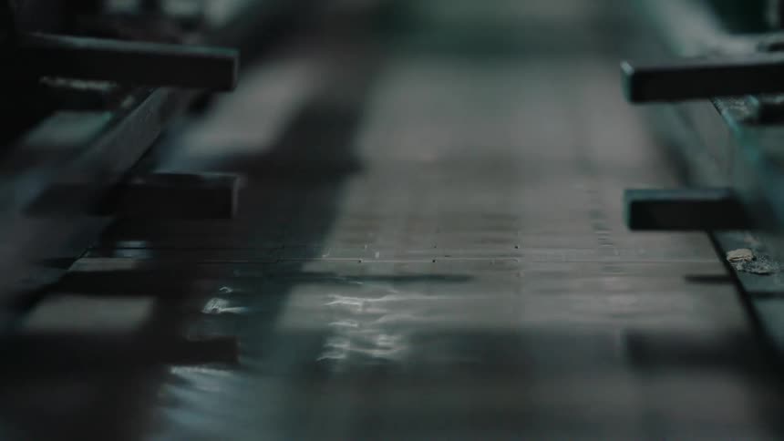 Water ripples and flows over a moving metal slat conveyor belt in a dark industrial facility