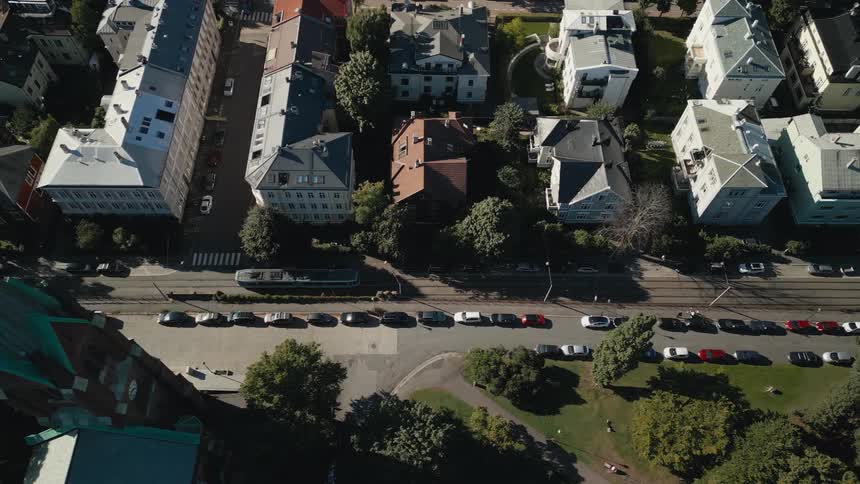 Top-down aerial shot following a tram on a European city street, pulling back to reveal a historic church steeple