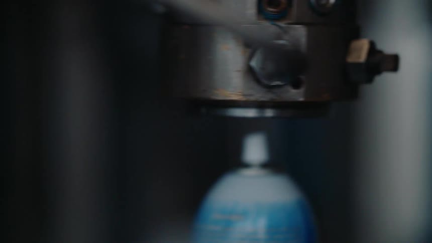 Automated machinery seals aerosol cans on a factory assembly line in a close-up shot