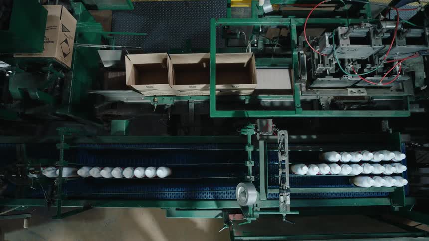 Top-down view of an automated factory production line packaging white bottles into cardboard boxes