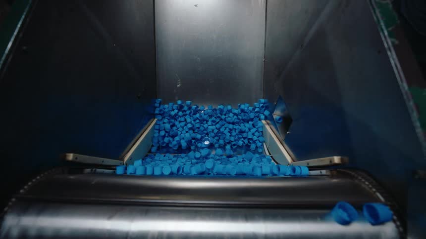 Close-up slow motion shot of blue plastic bottle caps moving up an assembly line in a factory