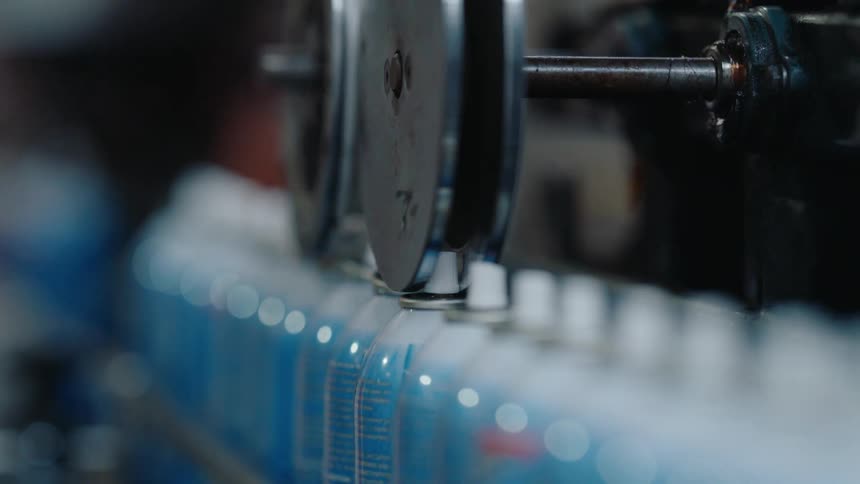 Slow motion close-up of aerosol cans moving along an automated production line in a factory