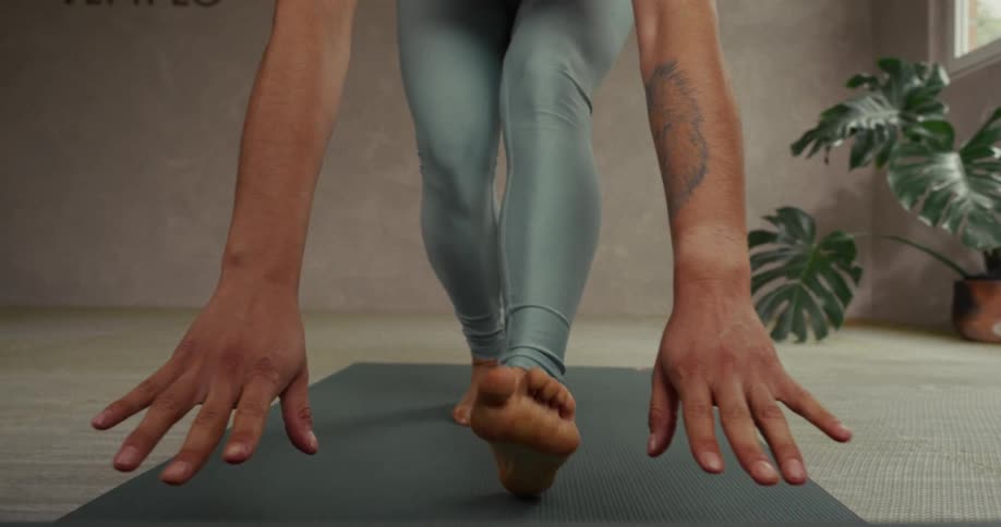A person's hands and feet are seen from a low-angle perspective as they slowly unroll a yoga mat in a studio