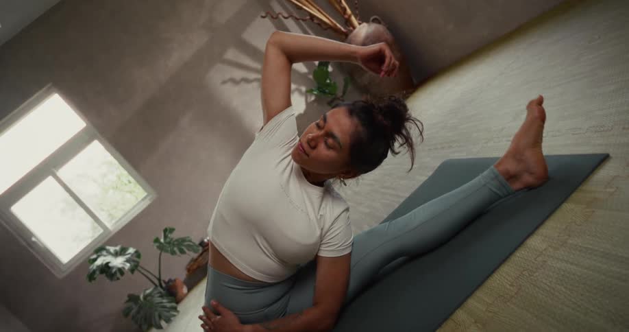 A woman gracefully executes a seated side bend yoga stretch, reaching for her foot in a serene studio