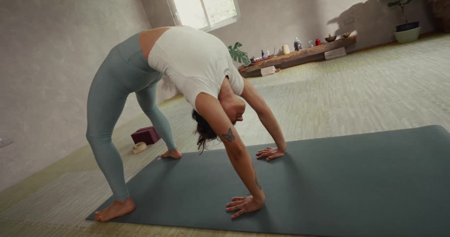 A flexible woman in a bright, tranquil studio gracefully performs a deep backbend yoga pose on her mat