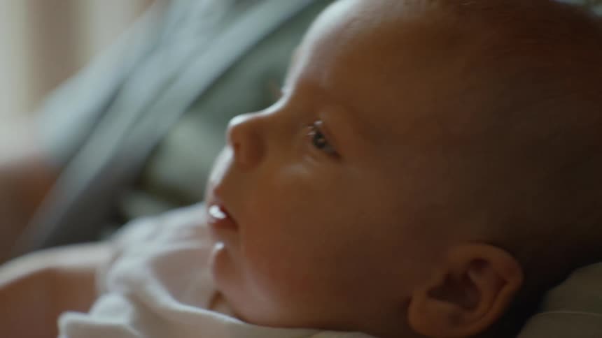A peaceful newborn baby with beautiful blue eyes looks around curiously in a softly lit room