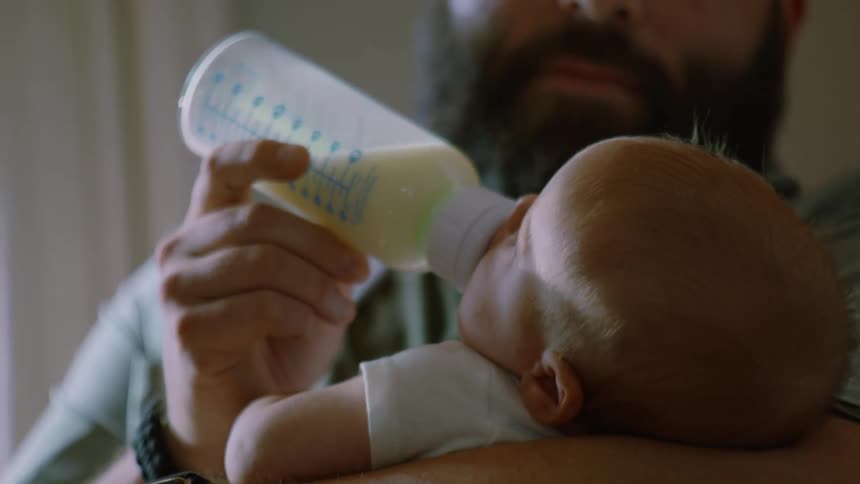 A close-up of a loving bearded father carefully feeding his newborn baby with a bottle of milk