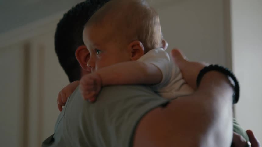 A loving father gently pats his newborn baby's back while holding them over his shoulder in a tender moment