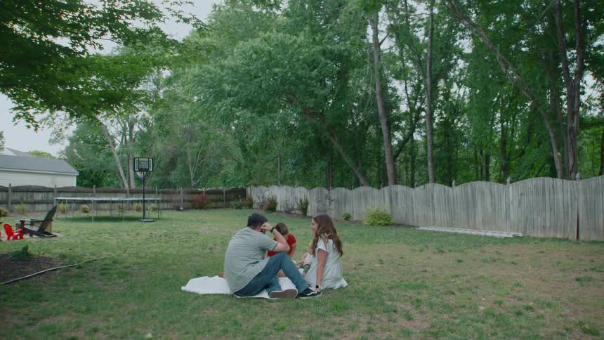 A young family spends quality time together, sitting on a blanket in their spacious backyard