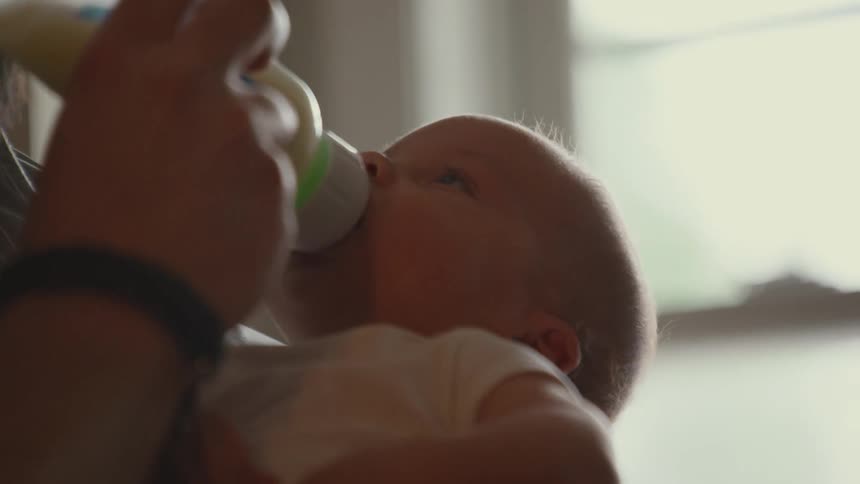 A parent tenderly holds and bottle-feeds their newborn baby in a softly lit room