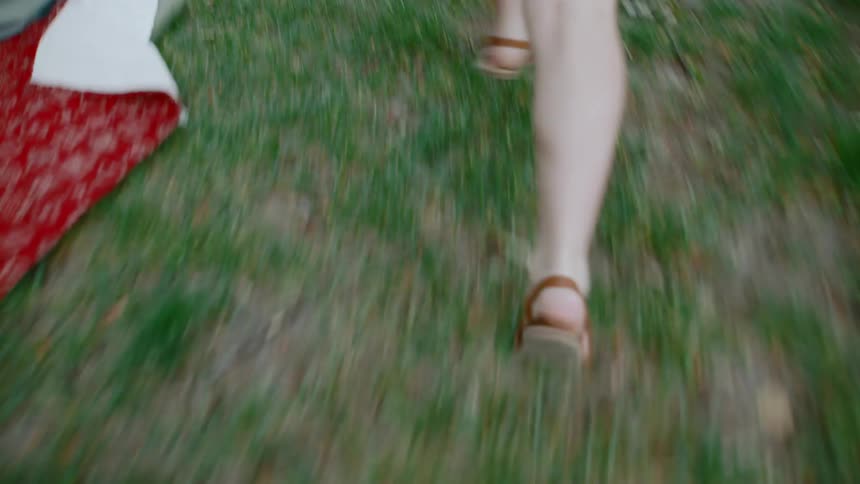 An energetic close-up shot follows a person's legs and feet as they run across a grassy lawn