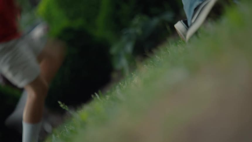 A blurry, low-angle shot captures the feet of several people as they walk across a green lawn