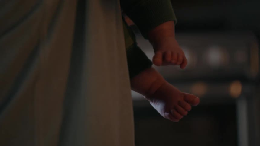 Close-up of a newborn baby's tiny bare feet as they are held by a parent in a softly lit room