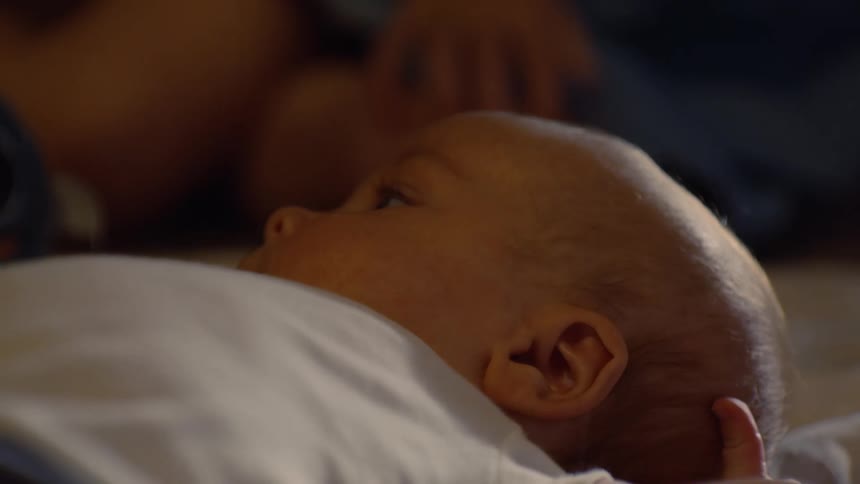 An intimate close-up shot of a newborn baby feeding from its mother's breast in a dimly lit room