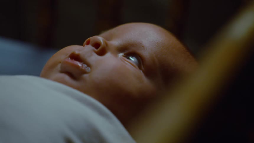 An intimate close-up of a peaceful newborn baby lying awake in their crib in a dimly lit room