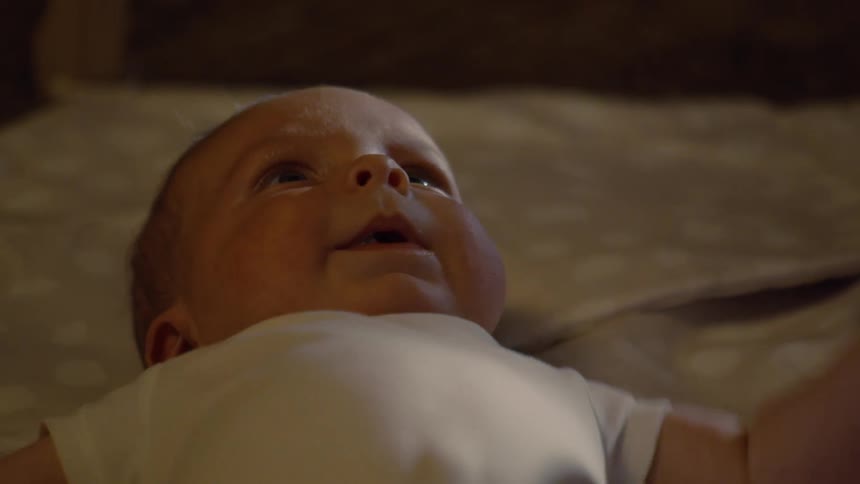 A peaceful newborn baby with blue eyes lies contentedly in a crib, curiously looking around