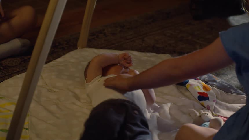 A tender sibling moment as a young girl gently strokes her baby brother lying on a play mat at home