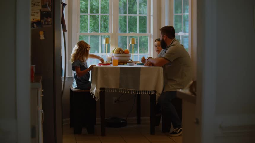 A father and his two young children enjoy a quiet breakfast together at the kitchen table in the morning light