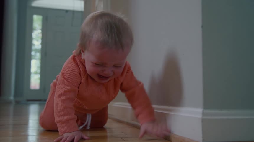 Upset baby boy crying crawling on the floor in a hallway at home