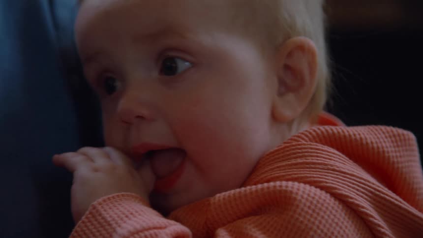 A close-up shot of a teary-eyed baby with their hand in their mouth, looking sad and fussy