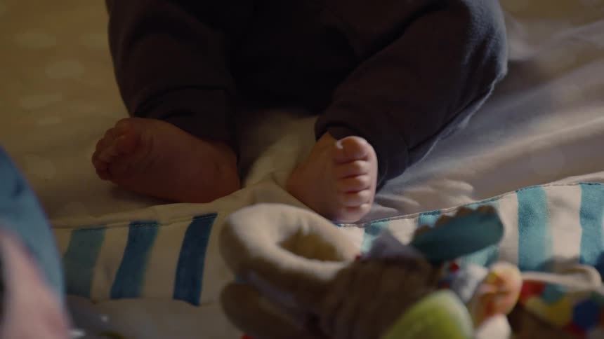 A close-up shot of a baby's tiny feet wiggling on a soft patterned blanket with a toy nearby