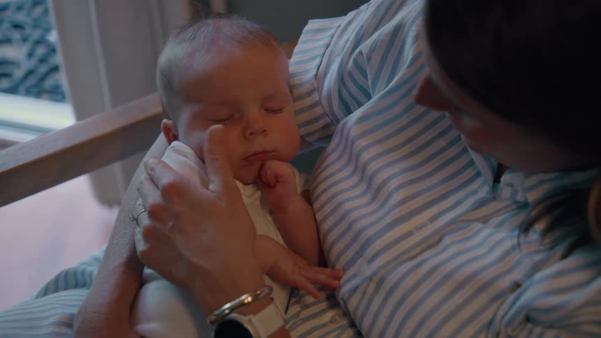 Close-up of a tender moment as a mother lovingly holds and caresses her sleeping newborn