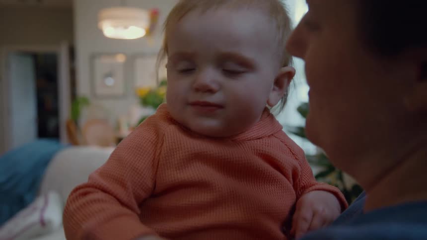 A happy baby in slow motion waves its hands and smiles while being held by its mother at home