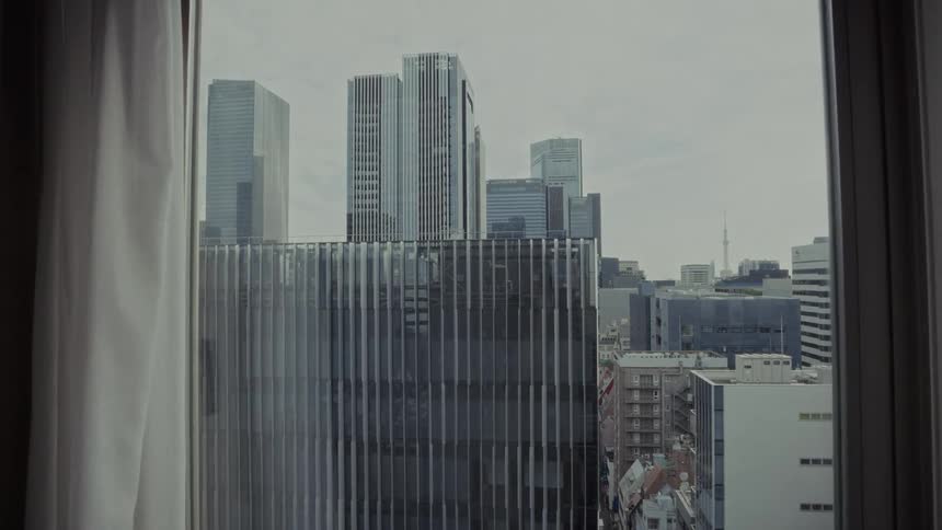 A cinematic view of the Tokyo city skyline with modern skyscrapers, seen through a hotel window on a cloudy day
