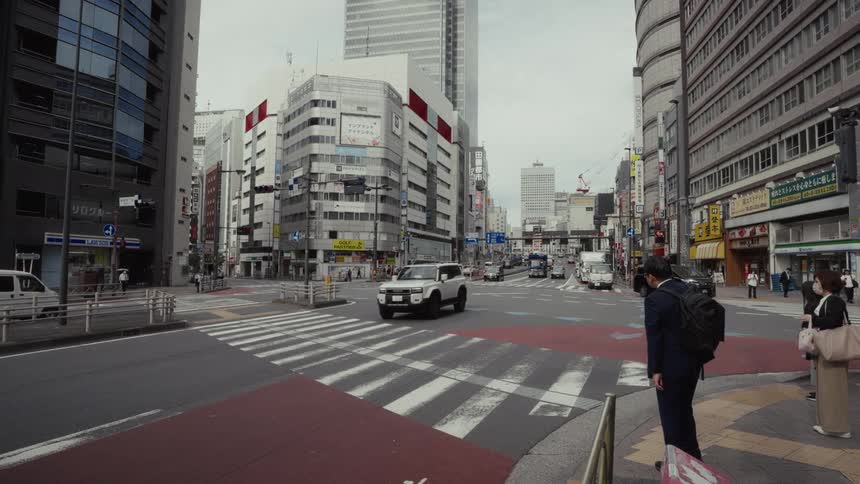 Cars drive through a modern intersection in Tokyo, Japan, as pedestrians wait on the sidewalk