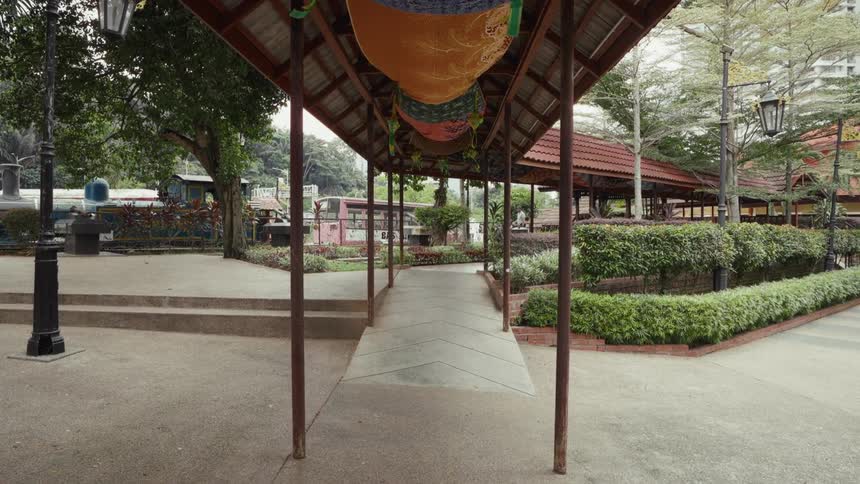 A decorated covered walkway leads through a serene public park with lush greenery and vintage trains on display