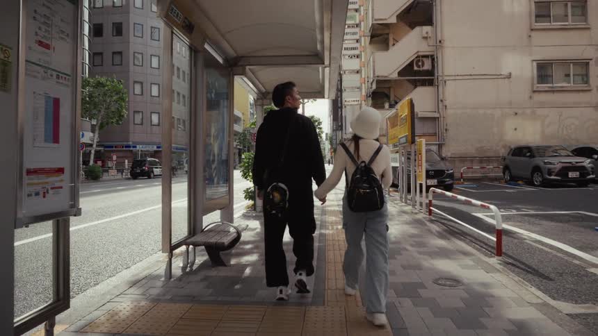 A young couple holds hands while walking down a sidewalk together in a modern Japanese city