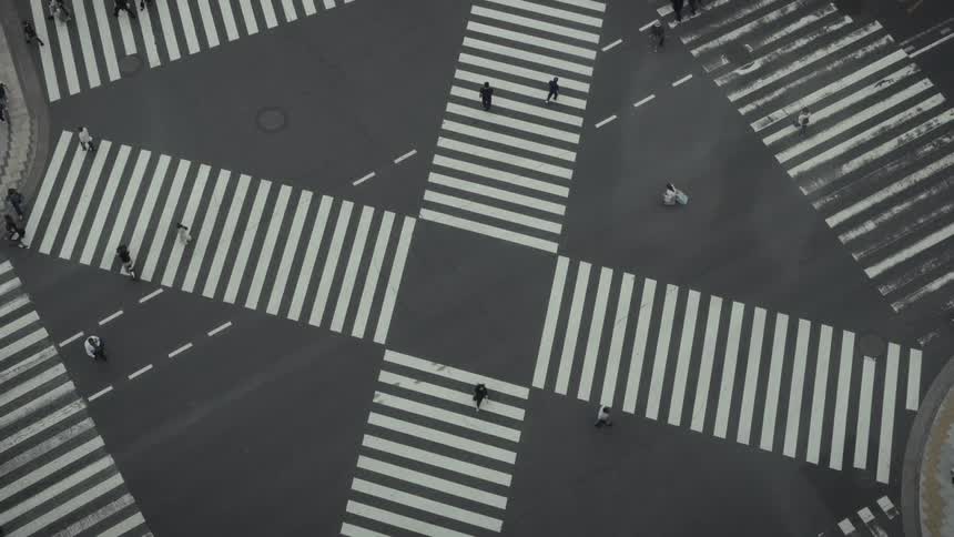 A high-angle, minimalist view shows pedestrians crossing a large, graphic street intersection
