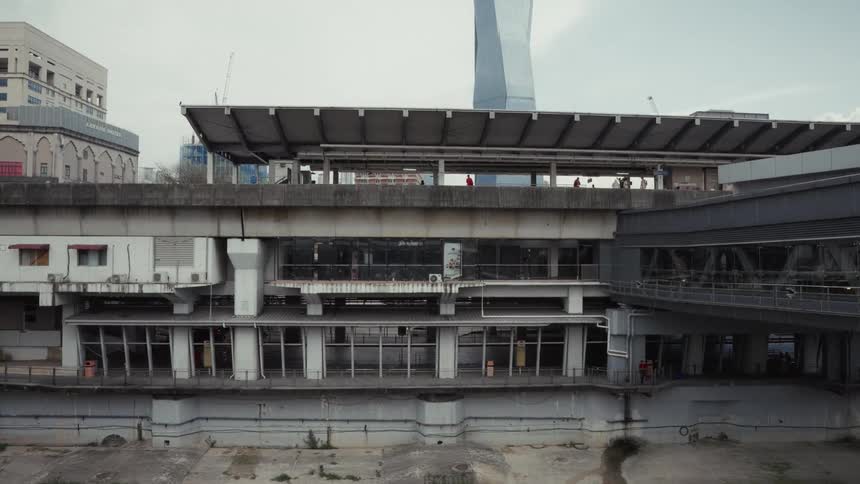 A weathered concrete train station stands in contrast to a modern skyscraper under an overcast sky in an urban landscape