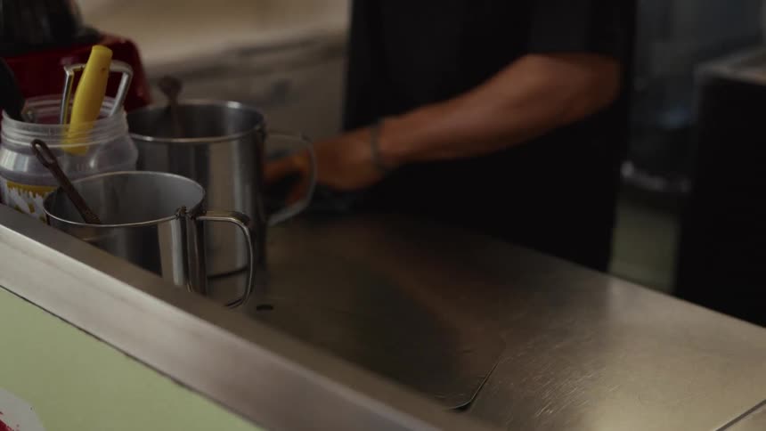 A kitchen worker meticulously wipes down a stainless steel countertop with a blue cloth in slow motion