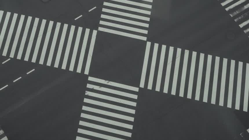 A minimalist top-down aerial shot captures two cars driving through a graphic city intersection with striking white crosswalks