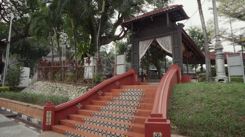 A beautiful red staircase with patterned tiles leads to a traditional wooden gateway in a tranquil park