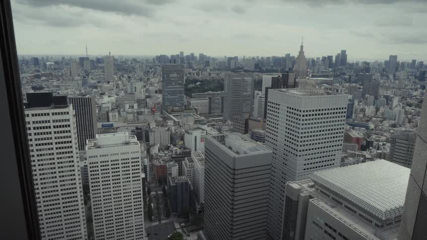An expansive, static high-angle view of the dense Tokyo cityscape under a gray, overcast sky