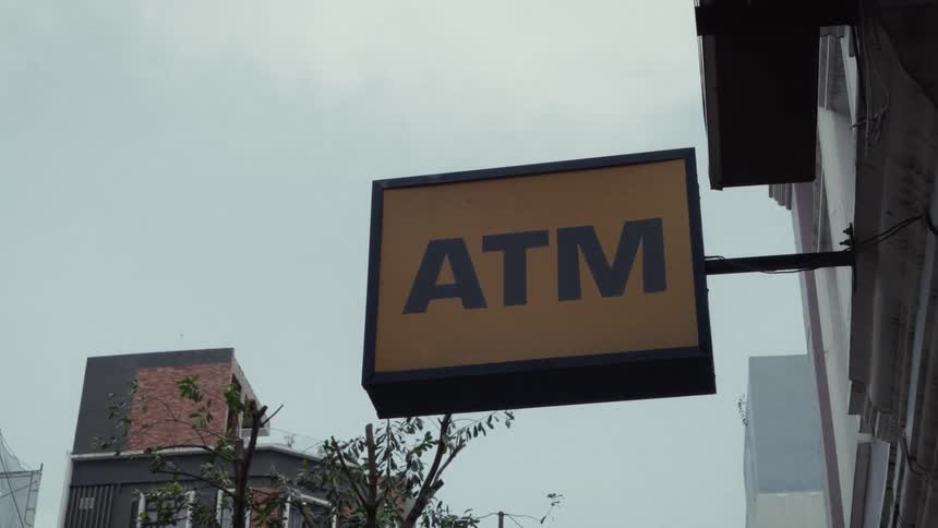 A yellow ATM sign hangs off the side of a building on a cloudy day in the city
