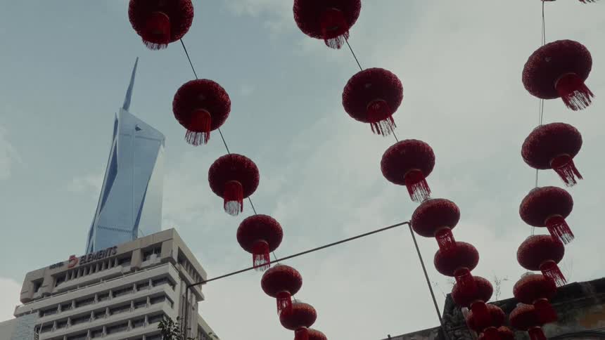 Red Chinese lanterns hang across a city street with a modern skyscraper rising into the sky behind them